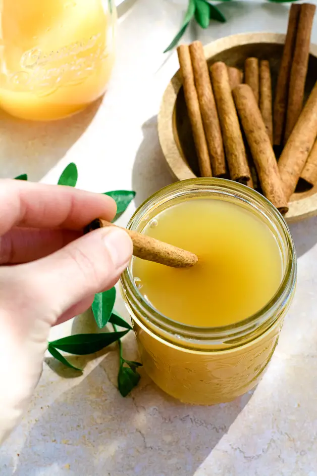 cinnamon stick being put into jar of apple cider vinegar