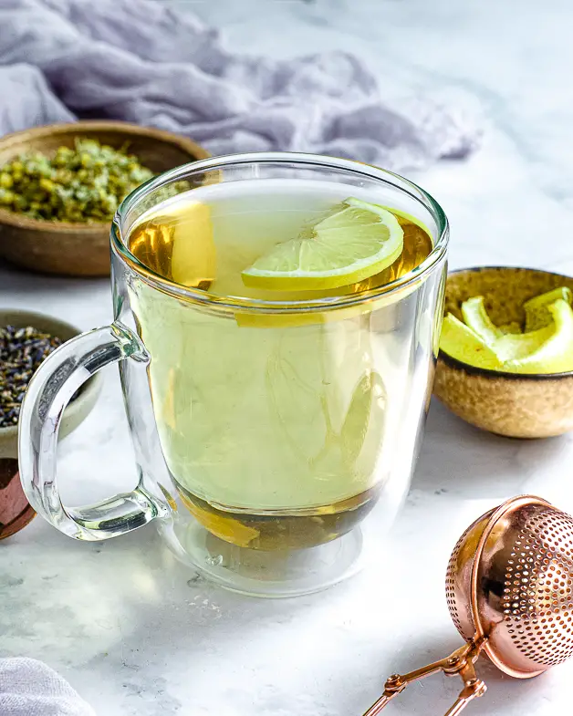 tea with lemon slices in a clear cup with lavender and chamomile in a bowl