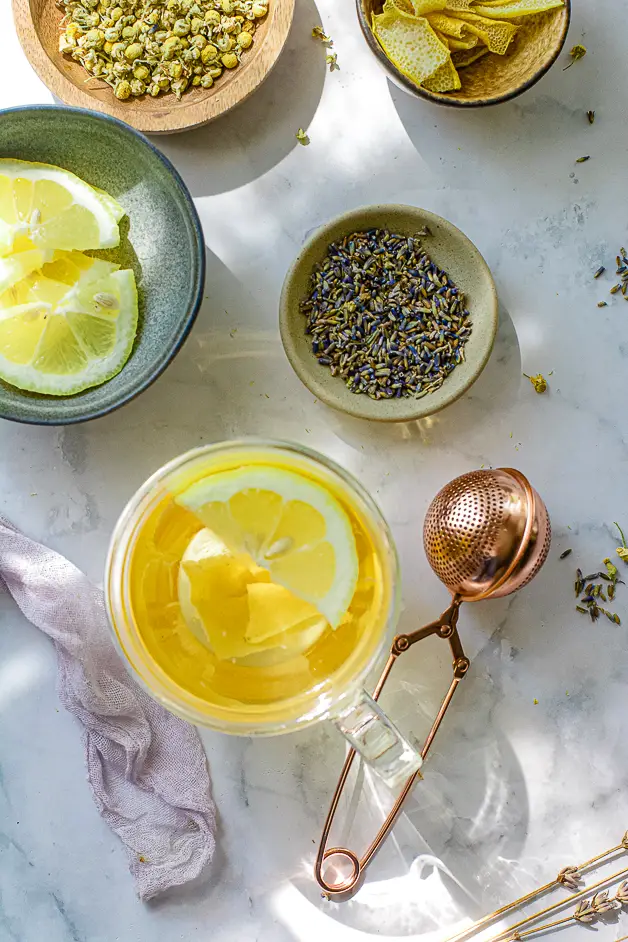 tea with lemon slices in a clear cup with lavender and chamomile in a bowl