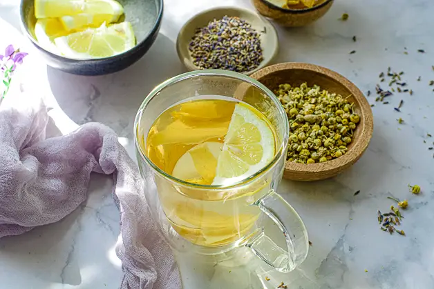 tea with lemon slices in a clear cup with lavender and chamomile in a bowl