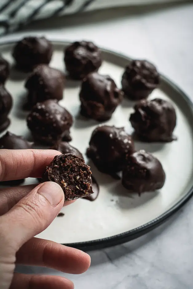 chocolate balls on a white plate and half bitten ball in hand