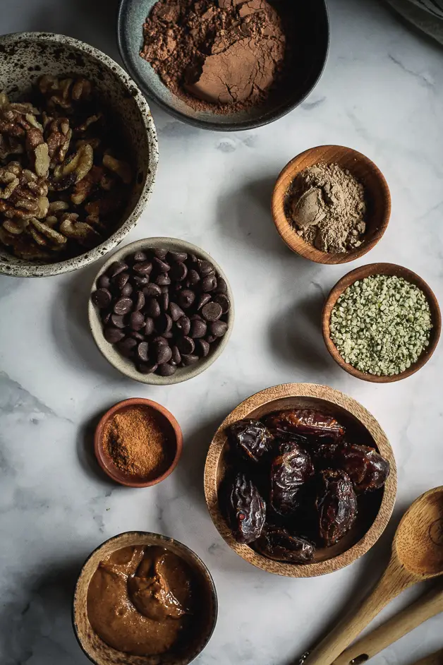 dates, chocolate chips, almond butter, walnuts, cacao on small bowls on a table