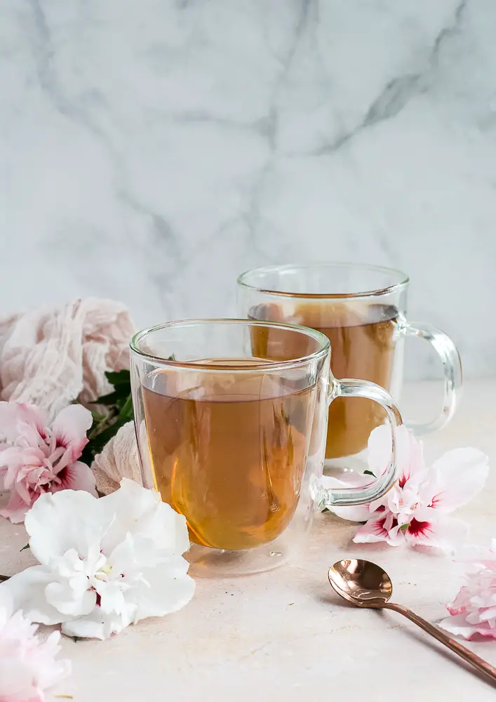 two cups of tea in clear cups on a table with hibiscus flowers