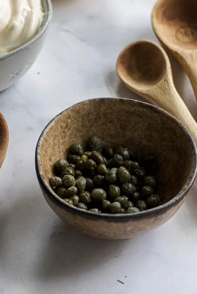 capers in a bowl with wooden spoons