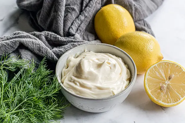 mayo in a bowl with lemons and a bunch of dill