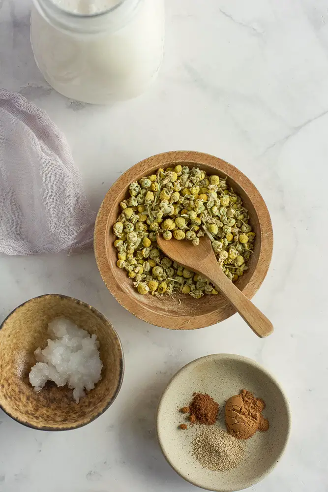 chamomile flowers in a small bowl, spices in a bowl and a white creamy oil coconut oil in a bowl.