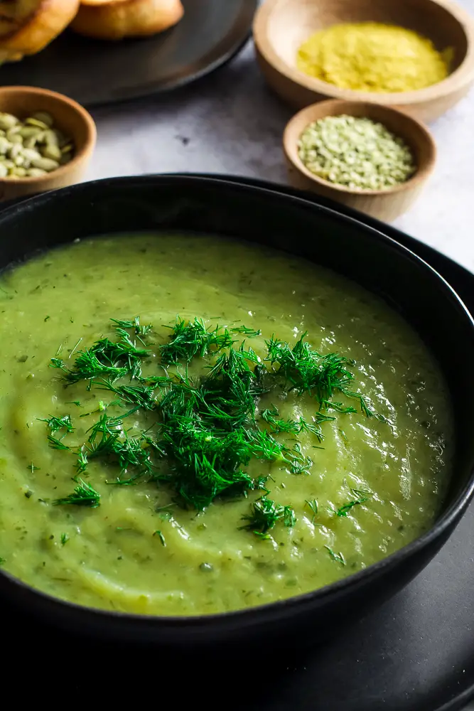 creamy green soup in a black bowl on a table with herbs on top