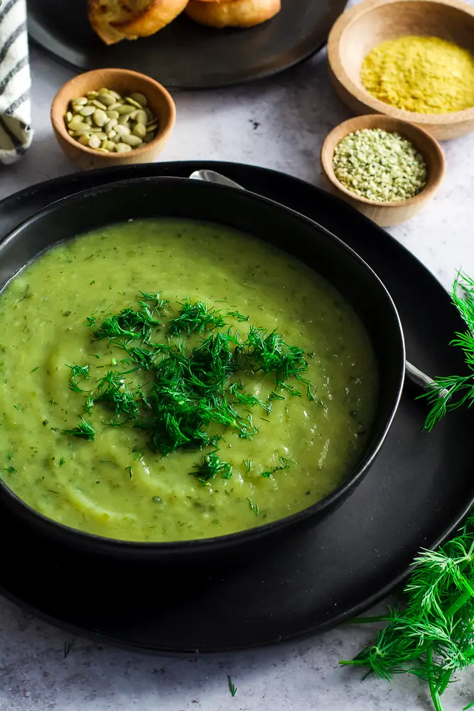creamy green soup in a black bowl on a table with herbs on top