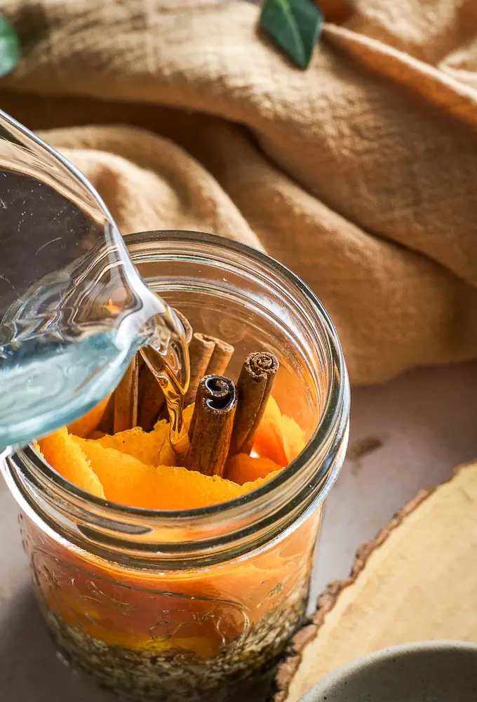 orange peels and cinnamon sticks in a jar being filled with liquid