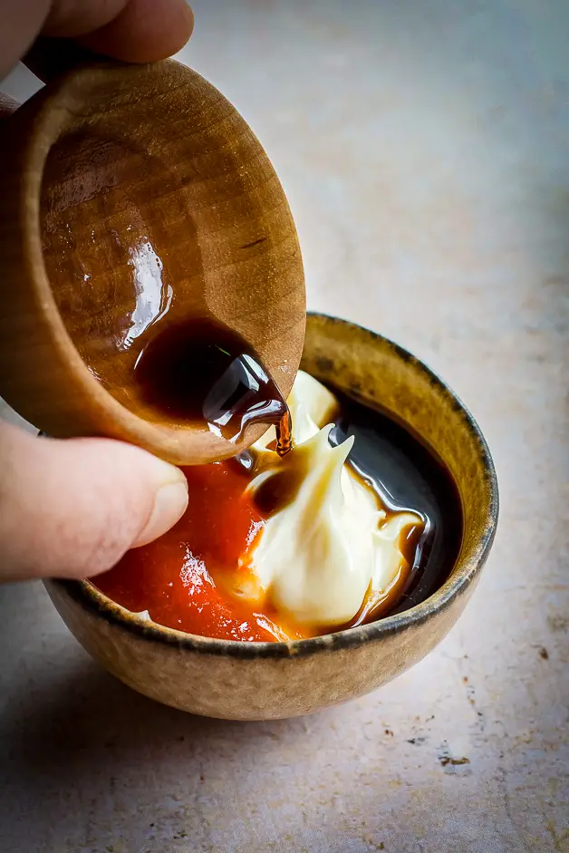 brown liquid being poured into a bowl with mayo sauce and red sauce 