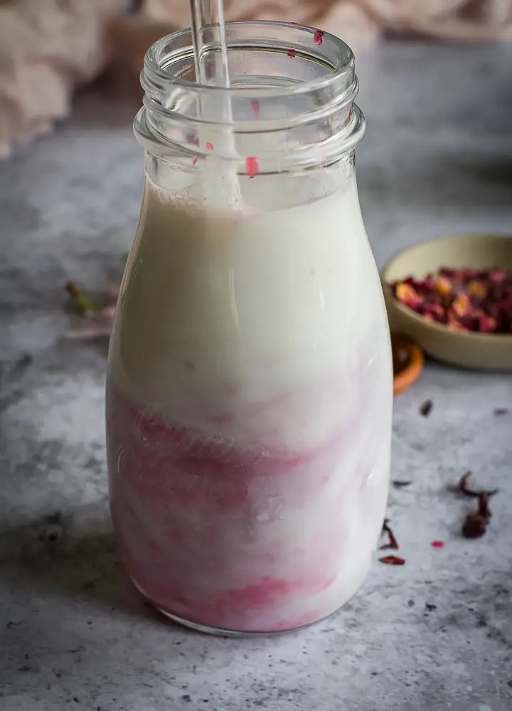 a jar of white liquid with some pink mixed into it with a straw