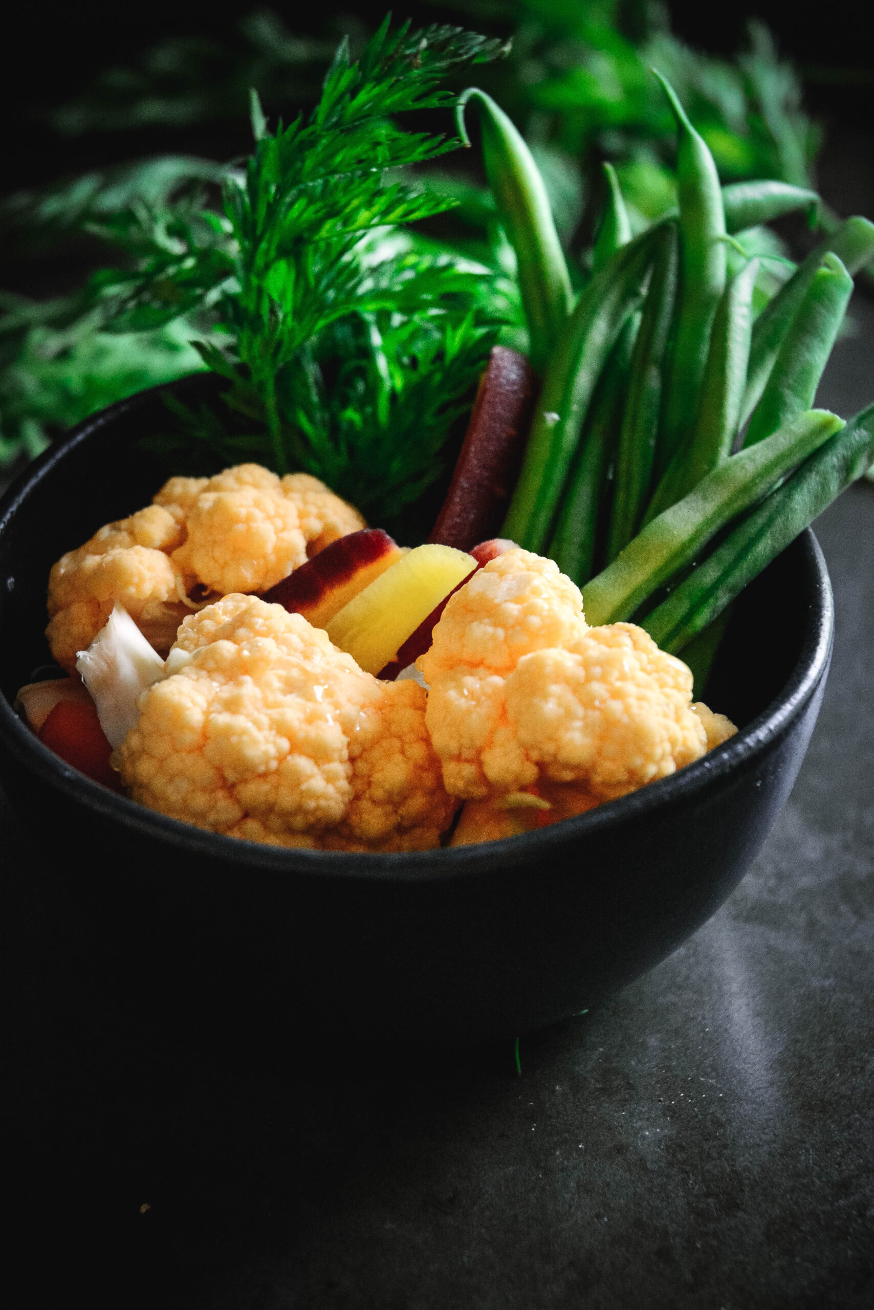 cauliflower, green beans, carrots and carrot tops in a small black bowl