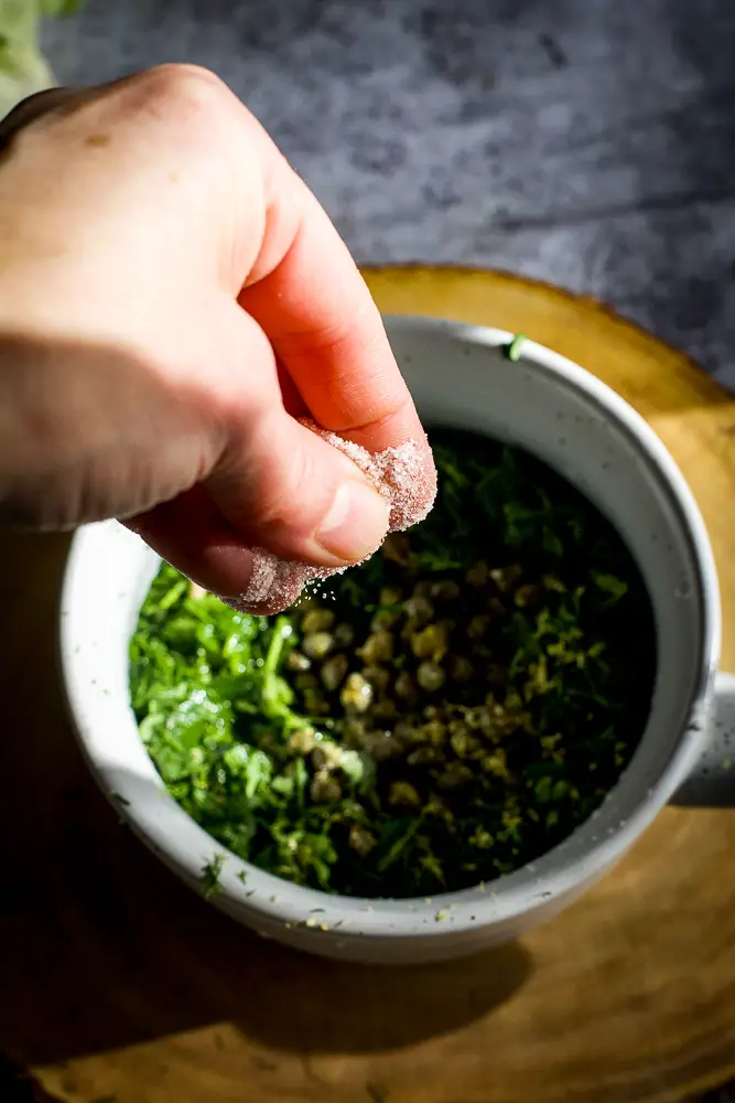 adding salt to a bowl of herbs